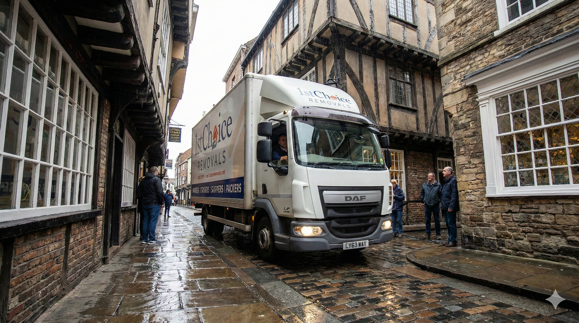 Truck driving down a narrow, cobbled street lined with historic buildings.