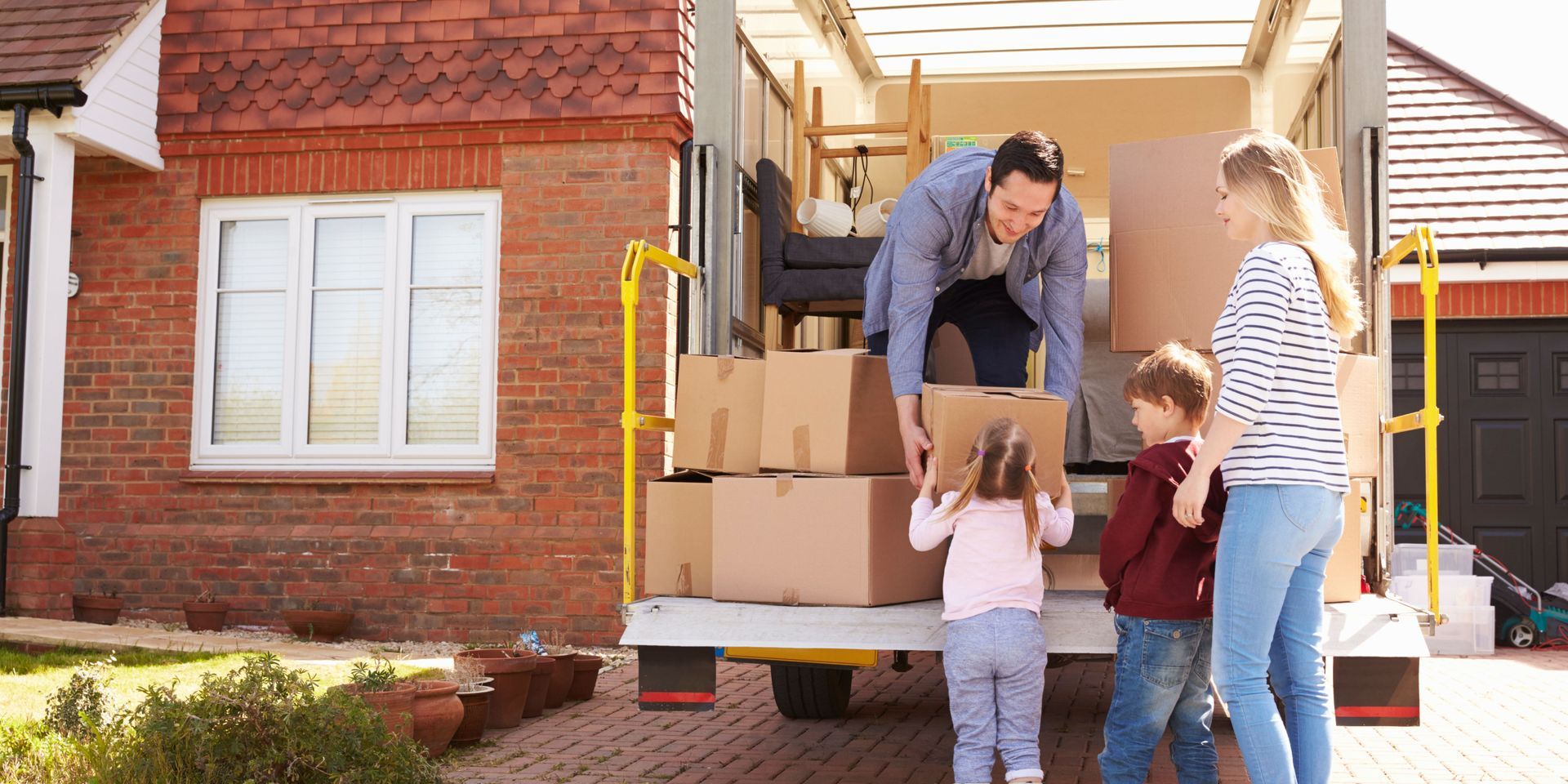 Family moving boxes into a truck in front of their new home.