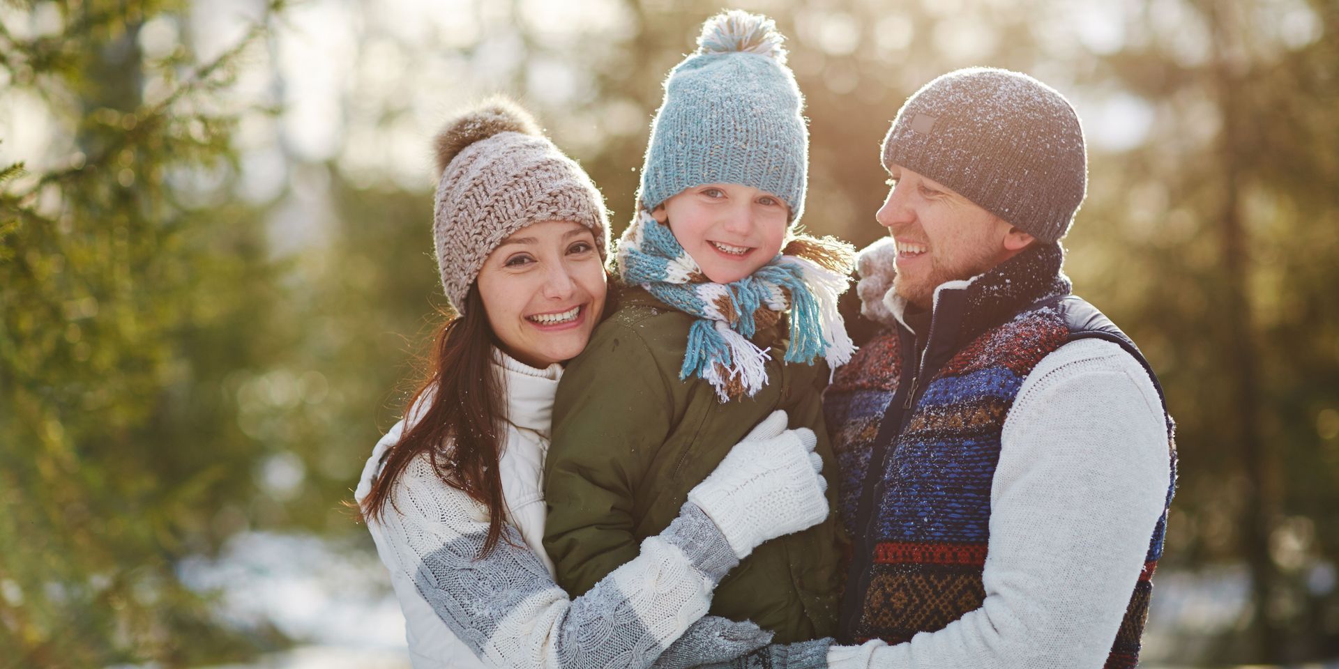 A family bundled up in winter clothing, smiling for a photo in a snowy, wooded area.