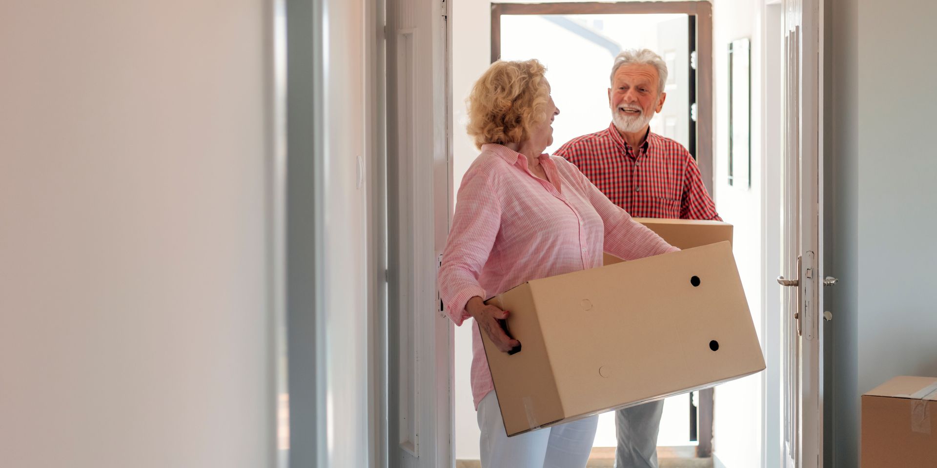 A man and a woman are carrying boxes into a new home.