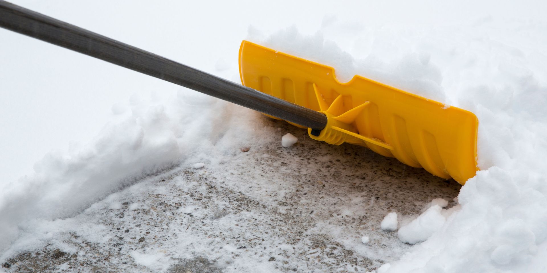 Yellow snow shovel clearing snow from a walkway.