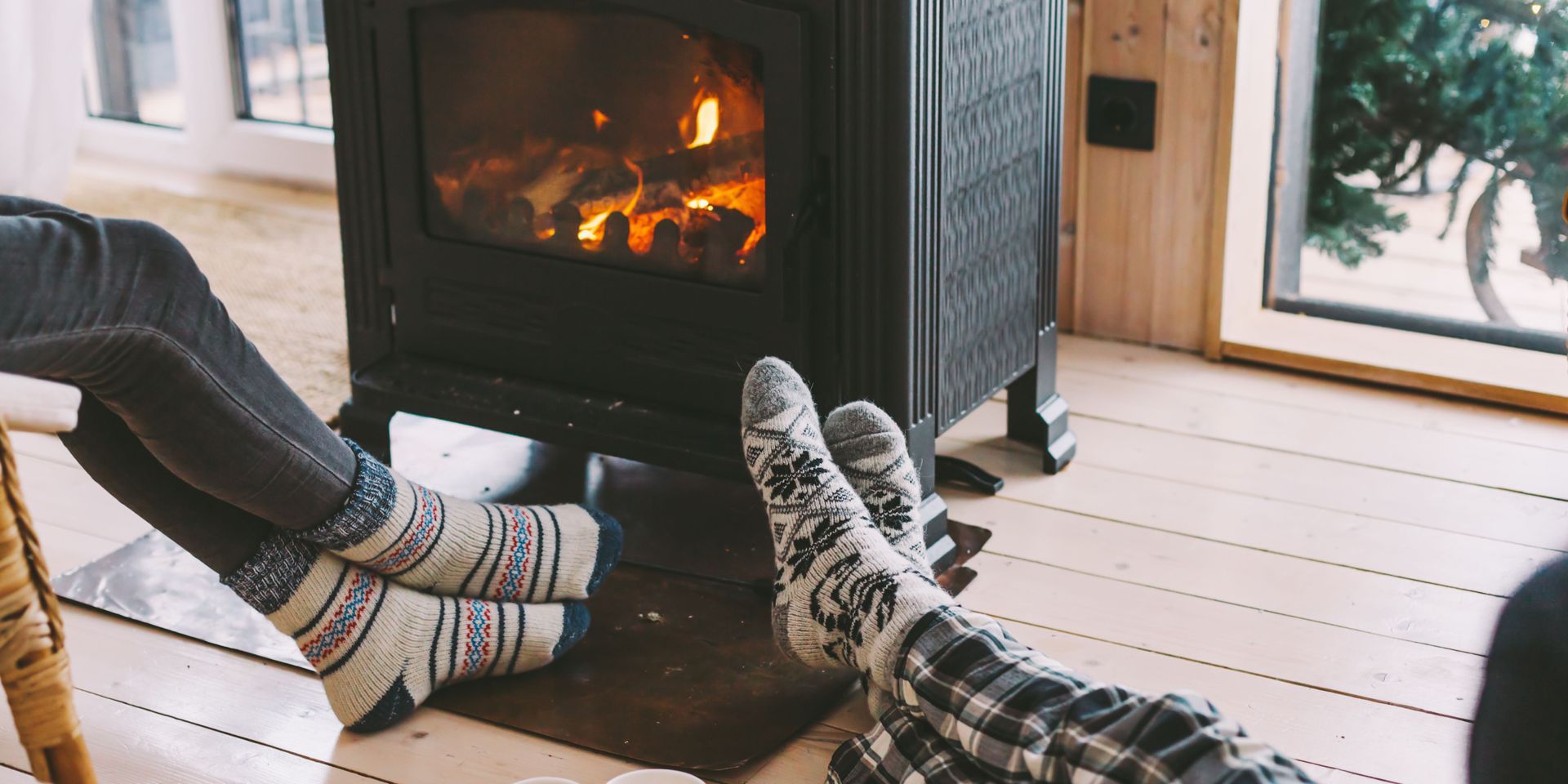 Cozy scene: feet in patterned socks warmed by a fireplace in a wooden-walled room.