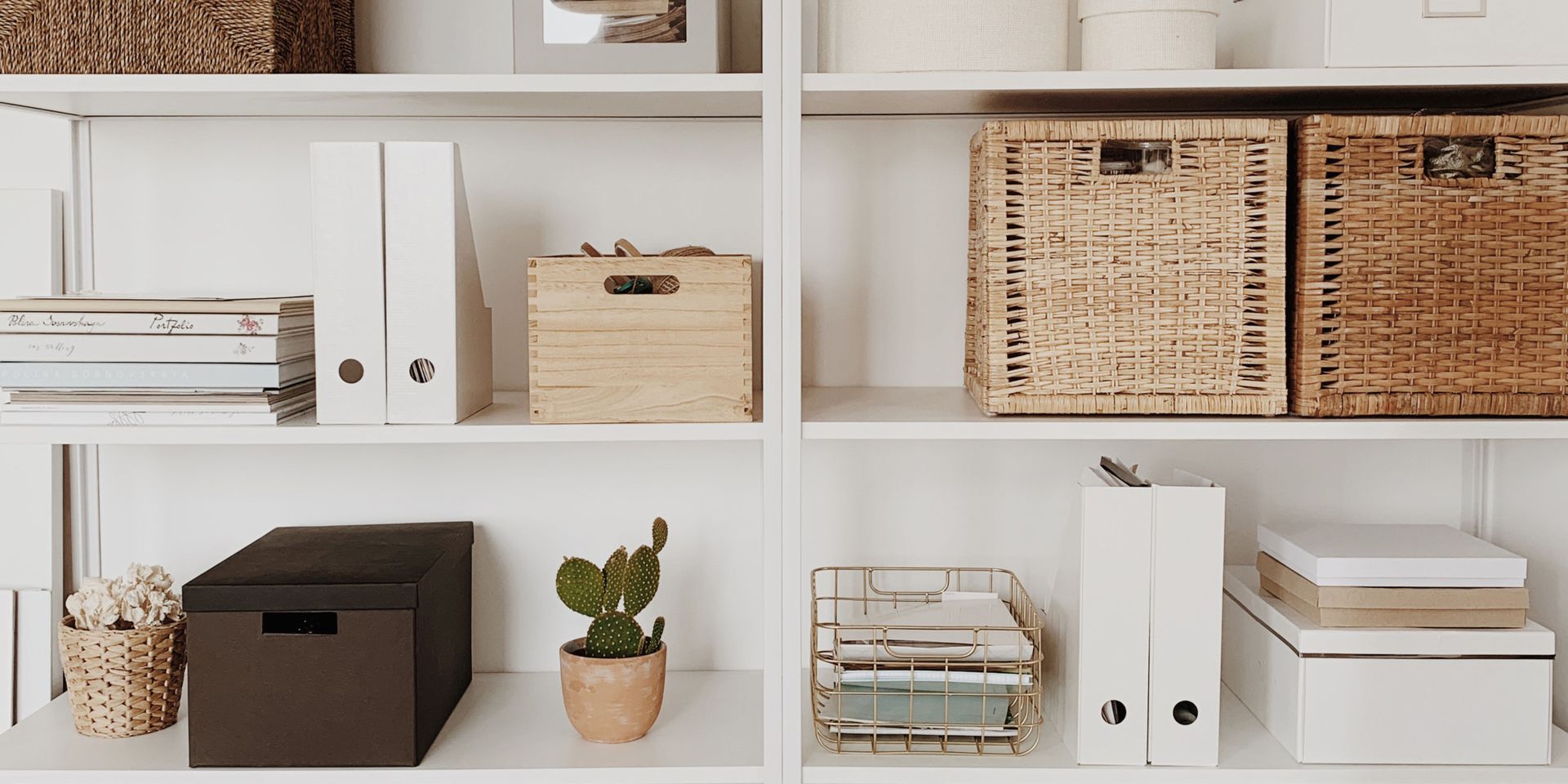 A shelf filled with boxes , baskets , books , and a cactus.