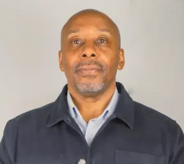 A man with a beard is wearing a blue jacket and a white shirt.