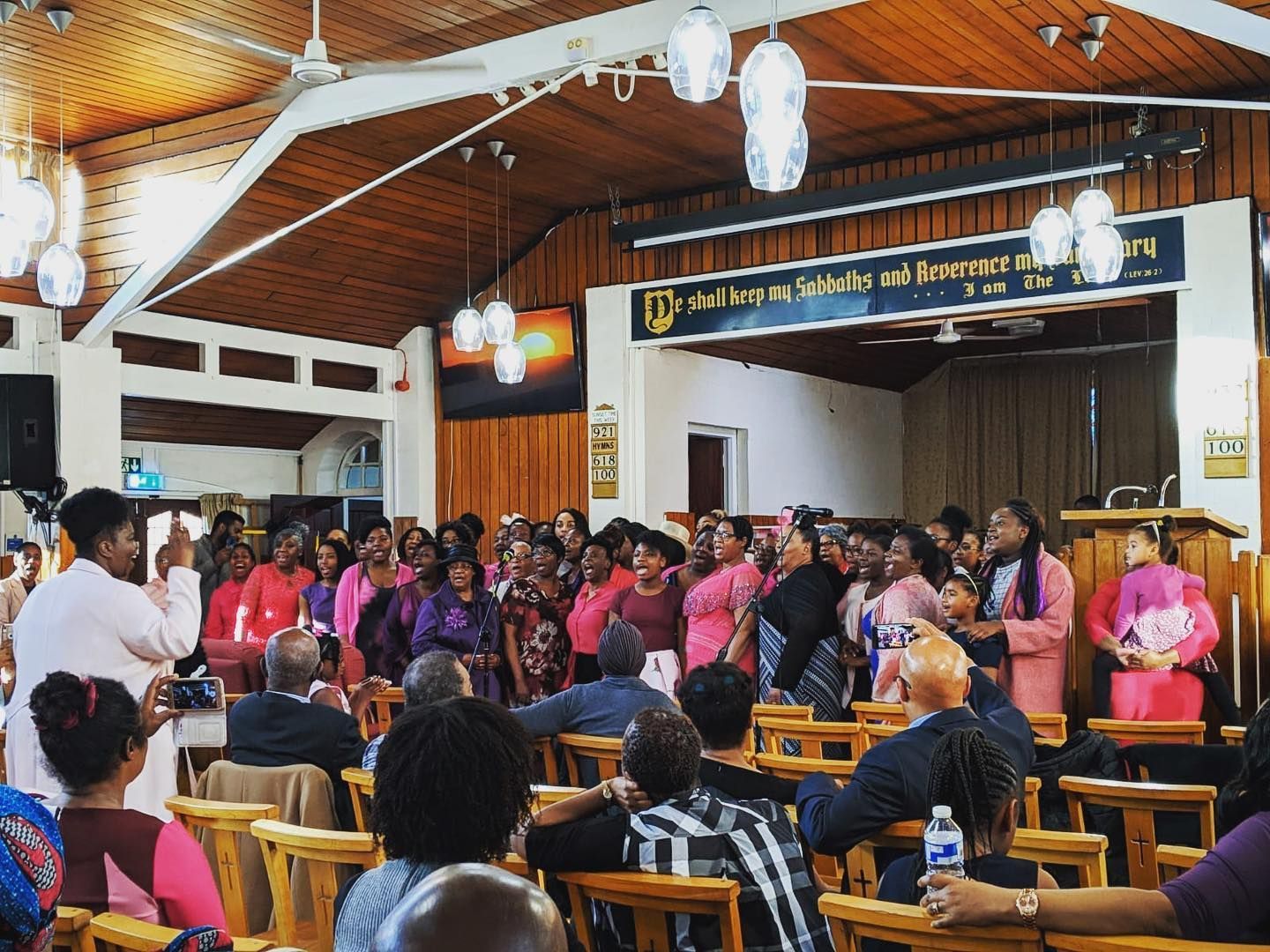 A large group of people are sitting in a church with a sign that says ' the islands of forgiveness ' on it