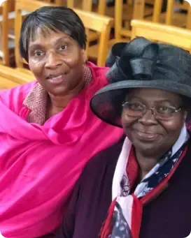 Two women wearing hats and scarves are sitting next to each other in a church.