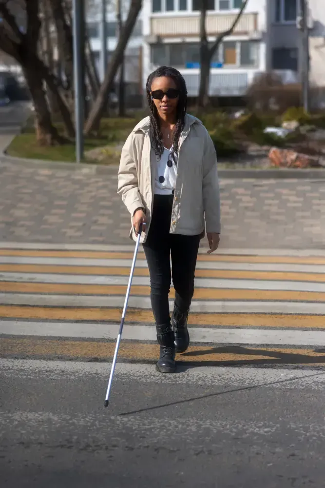 A blind woman is crossing the street with a cane.