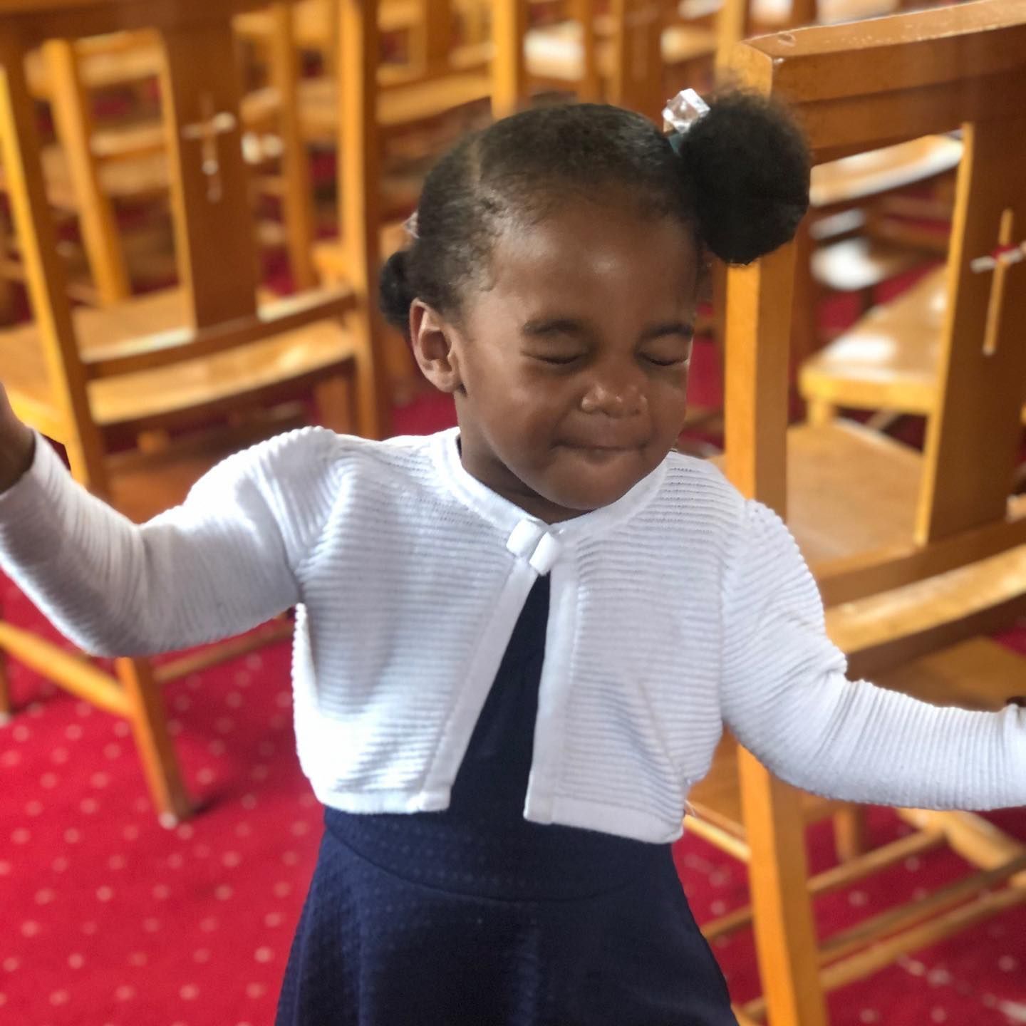 A little girl wearing a white cardigan and a blue dress