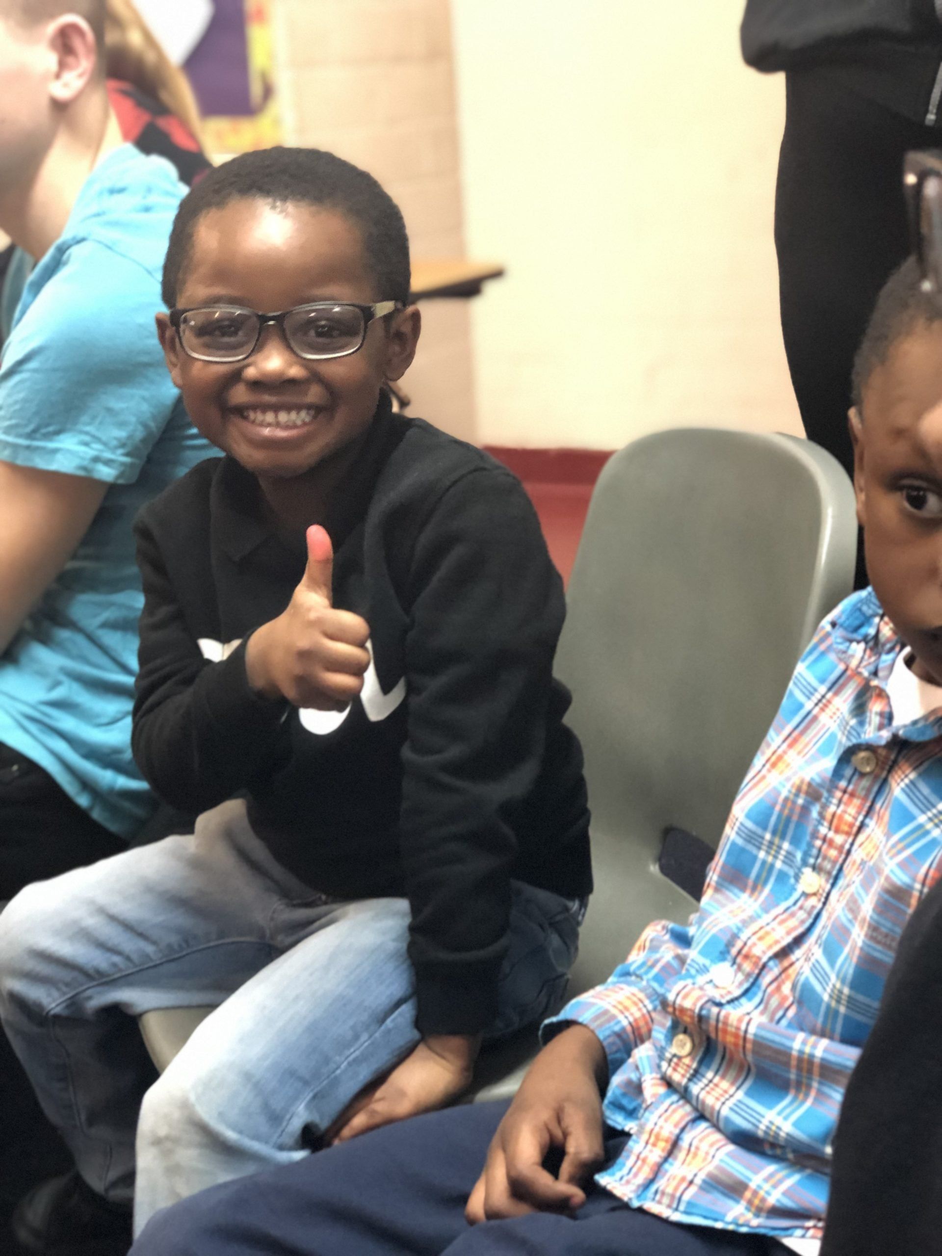 A young boy wearing glasses is giving a thumbs up