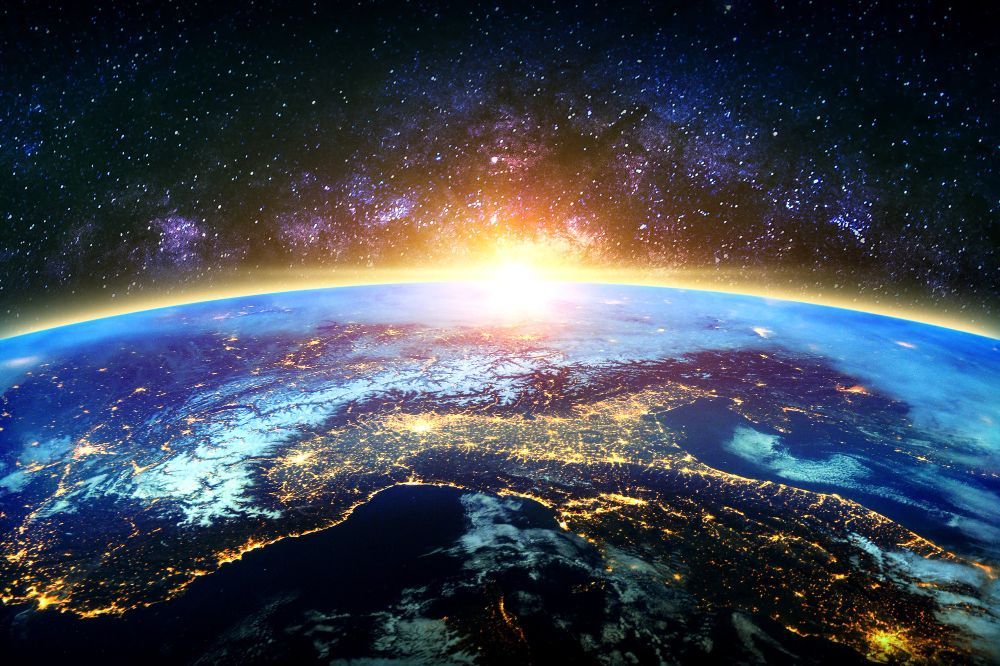 A view of the earth from space at night with the sun rising over it.