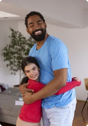 A man is hugging a little girl in a living room