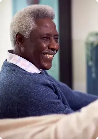 A man with gray hair is sitting on a couch and smiling.