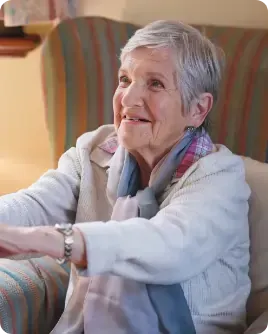 An elderly woman is sitting in a chair with her arms outstretched.