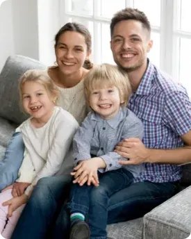 A family is sitting on a couch and smiling for the camera.