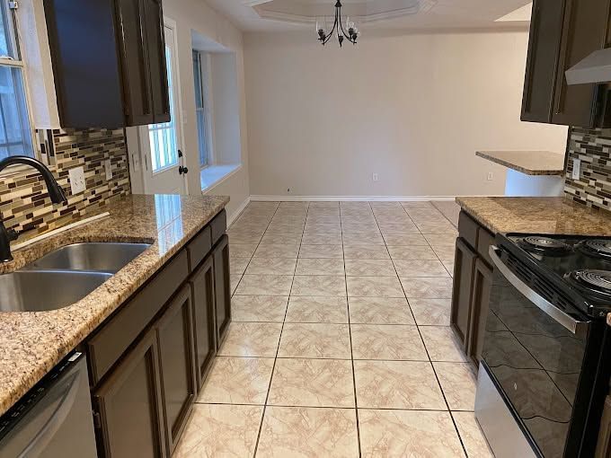 Empty kitchen with tan tile floor, dark cabinets, granite counters, and a small dining area in the back.