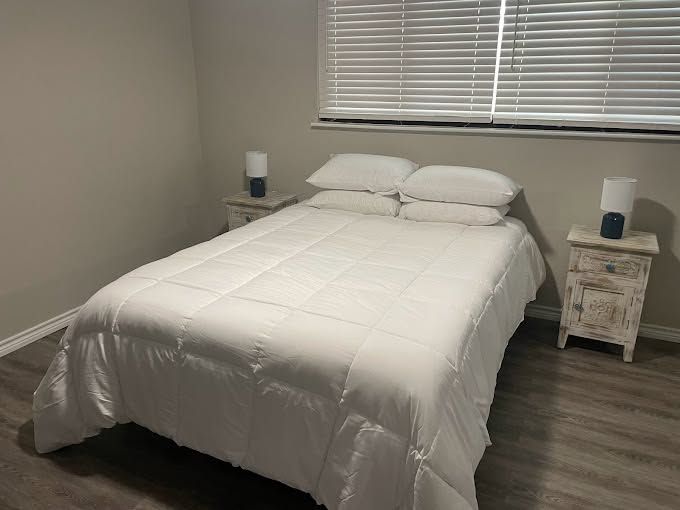 Neatly made bed with white bedding in a simple bedroom, flanked by two matching nightstands and lamps.