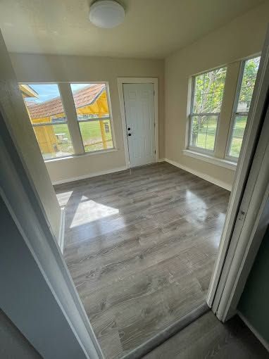 Empty bright room with gray wood-look floor, white walls, and large windows