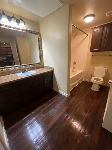 Bathroom with dark wood vanity, large mirror, and toilet beside a tub in warm lighting.