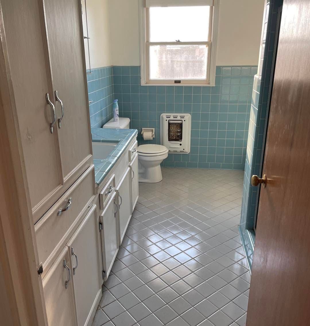 Narrow vintage bathroom with blue tile, white sink and toilet, and a window above the toilet.