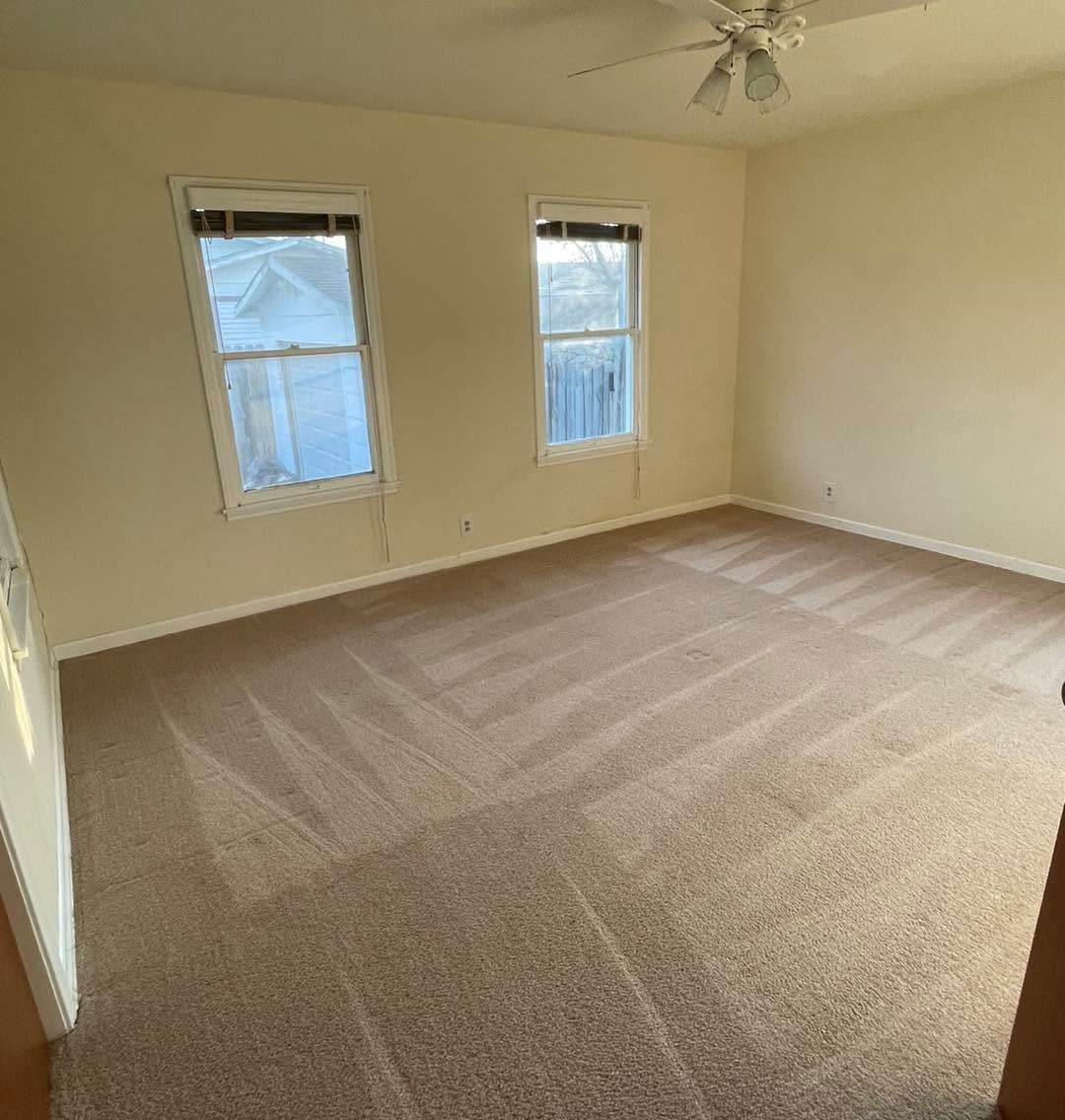 Empty beige carpeted bedroom with two windows and a ceiling fan