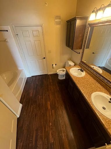 Small beige bathroom with dark wood vanity, mirror, sink, toilet, and closed white door.