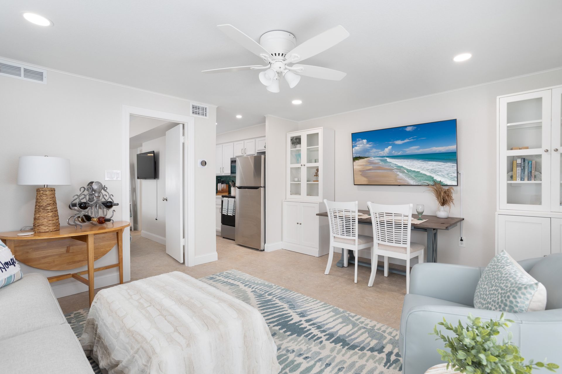 Bright airy living room with white furniture, ceiling fan, dining table, and beach wall art
