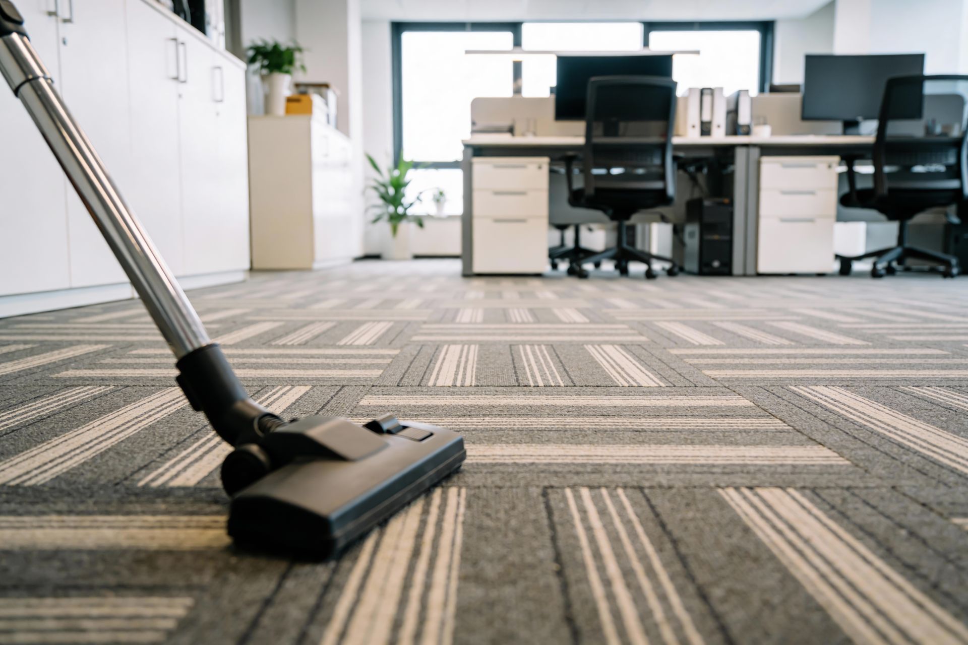 Vacuum cleaner on carpet in a modern office with desks and chairs behind it