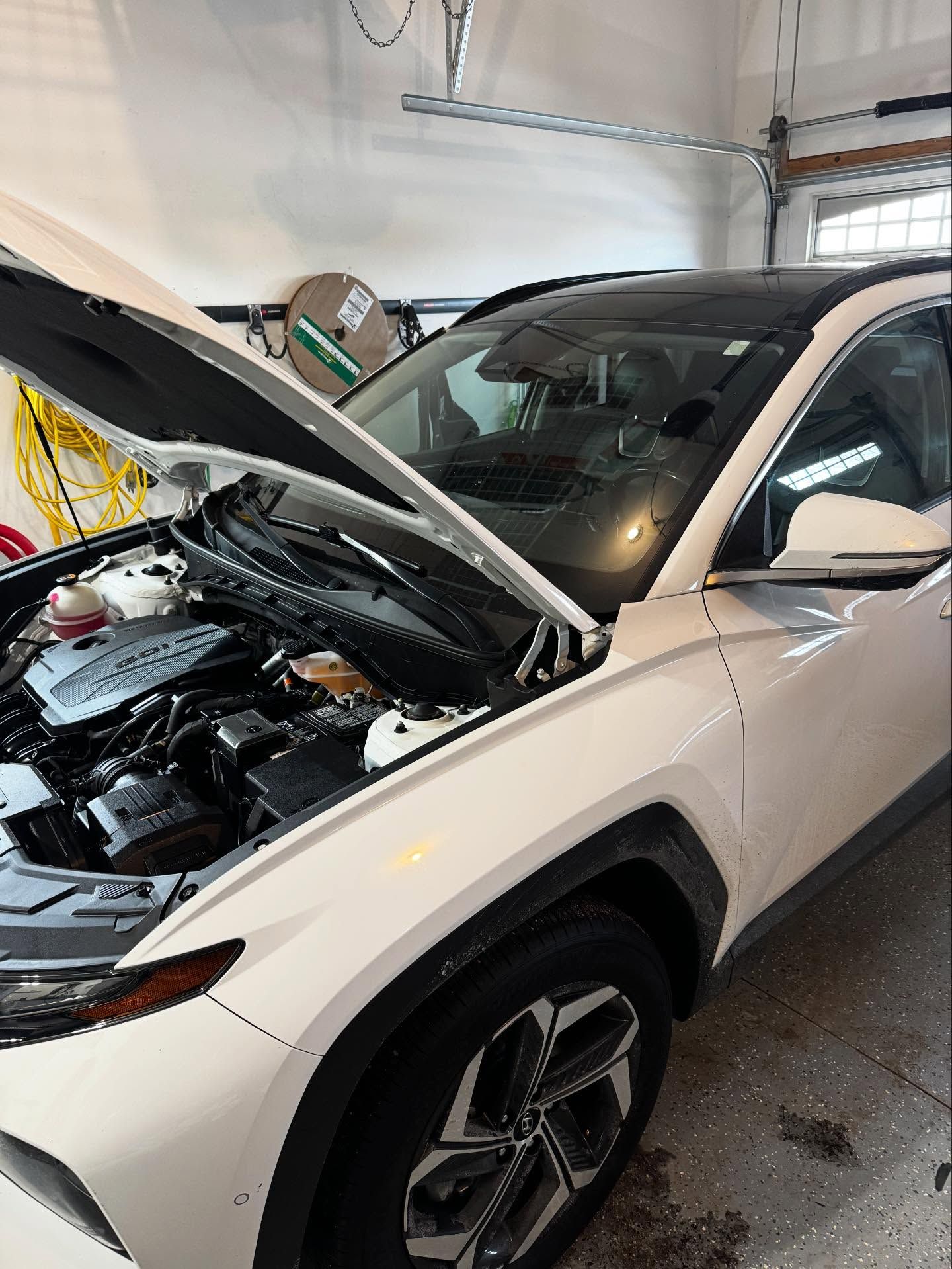 A white SUV parked in a garage with its hood open, exposing the engine bay.