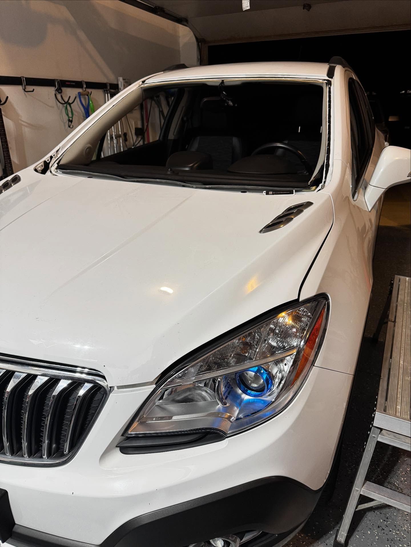 White car parked in a garage with its windshield missing and the frame exposed.