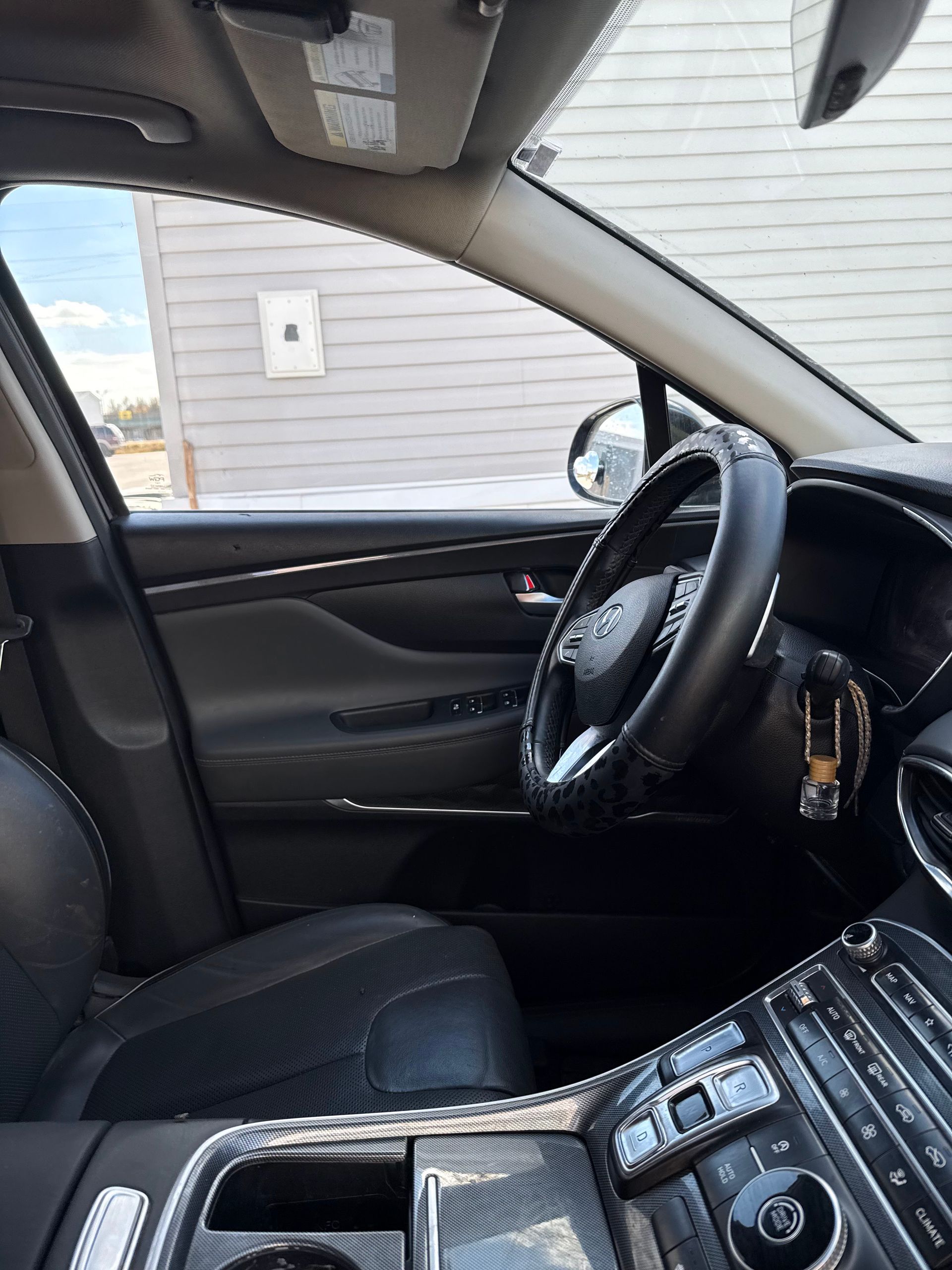 Interior view of a car cockpit featuring a black leather steering wheel, dark upholstery, and a wood-grain center console.