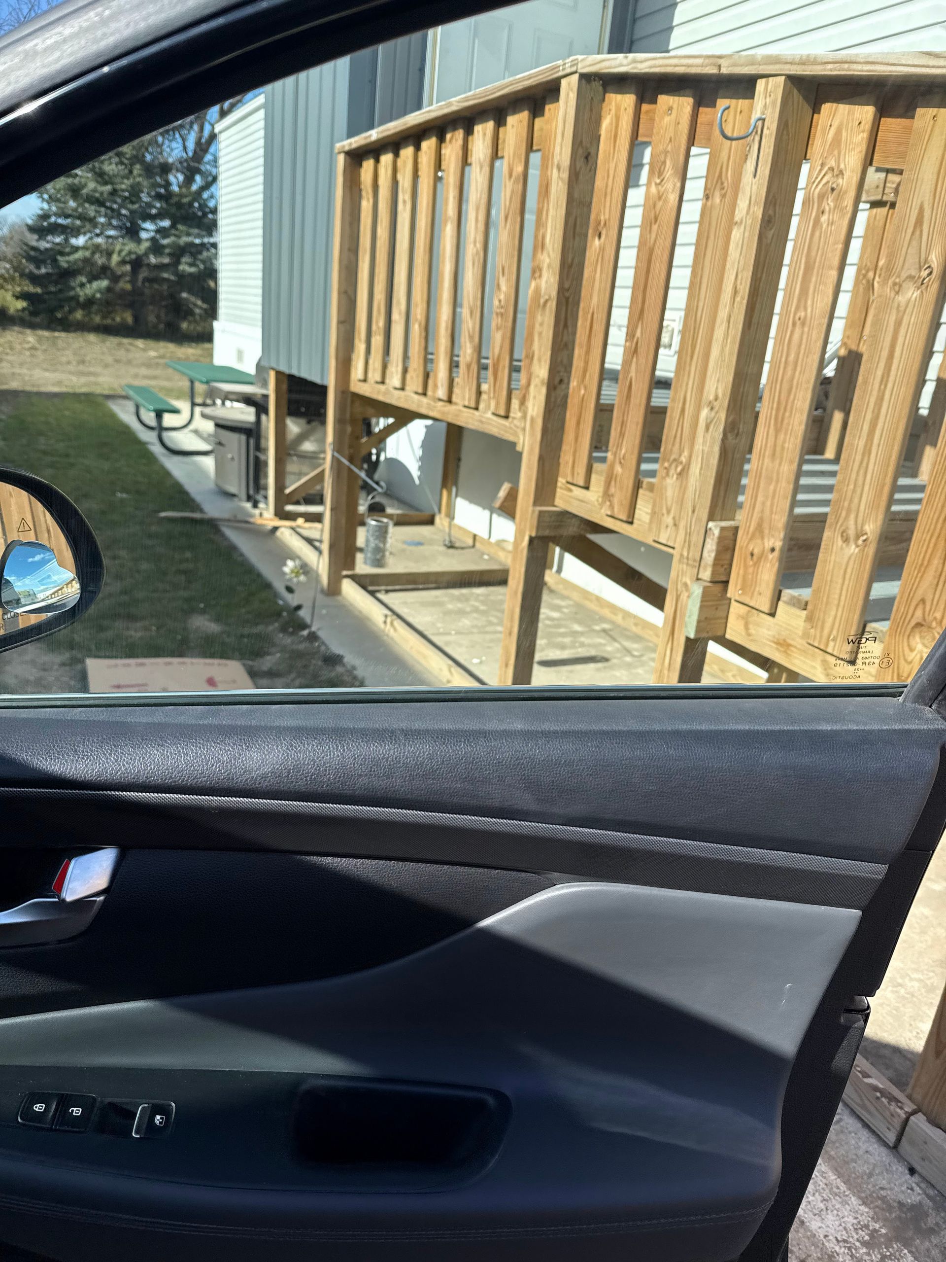 A view from inside a car looking out at a wooden deck attached to a house on a sunny day.