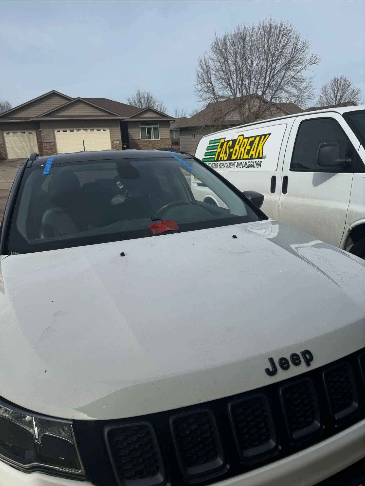 A white Jeep parked next to a white work van with green and yellow logo text in a residential driveway.
