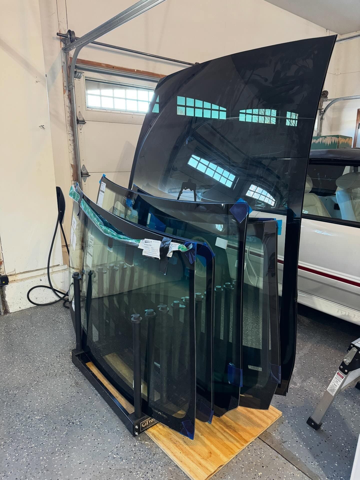 A storage rack in a garage holding several stacked automotive windshields and glass panels.