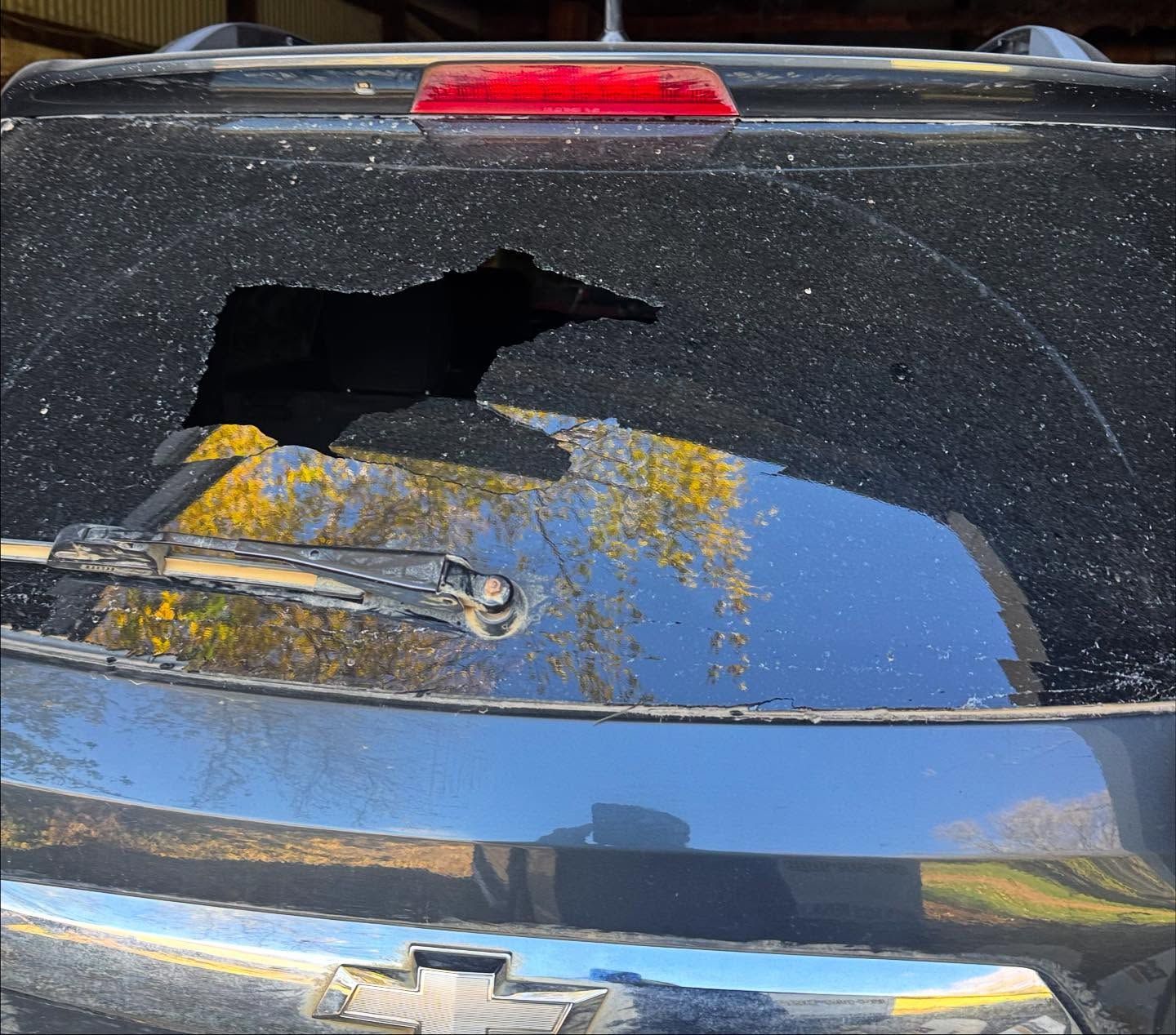 A close-up view of the rear window of a black Chevrolet SUV with a large jagged hole smashed into the center of the glass.