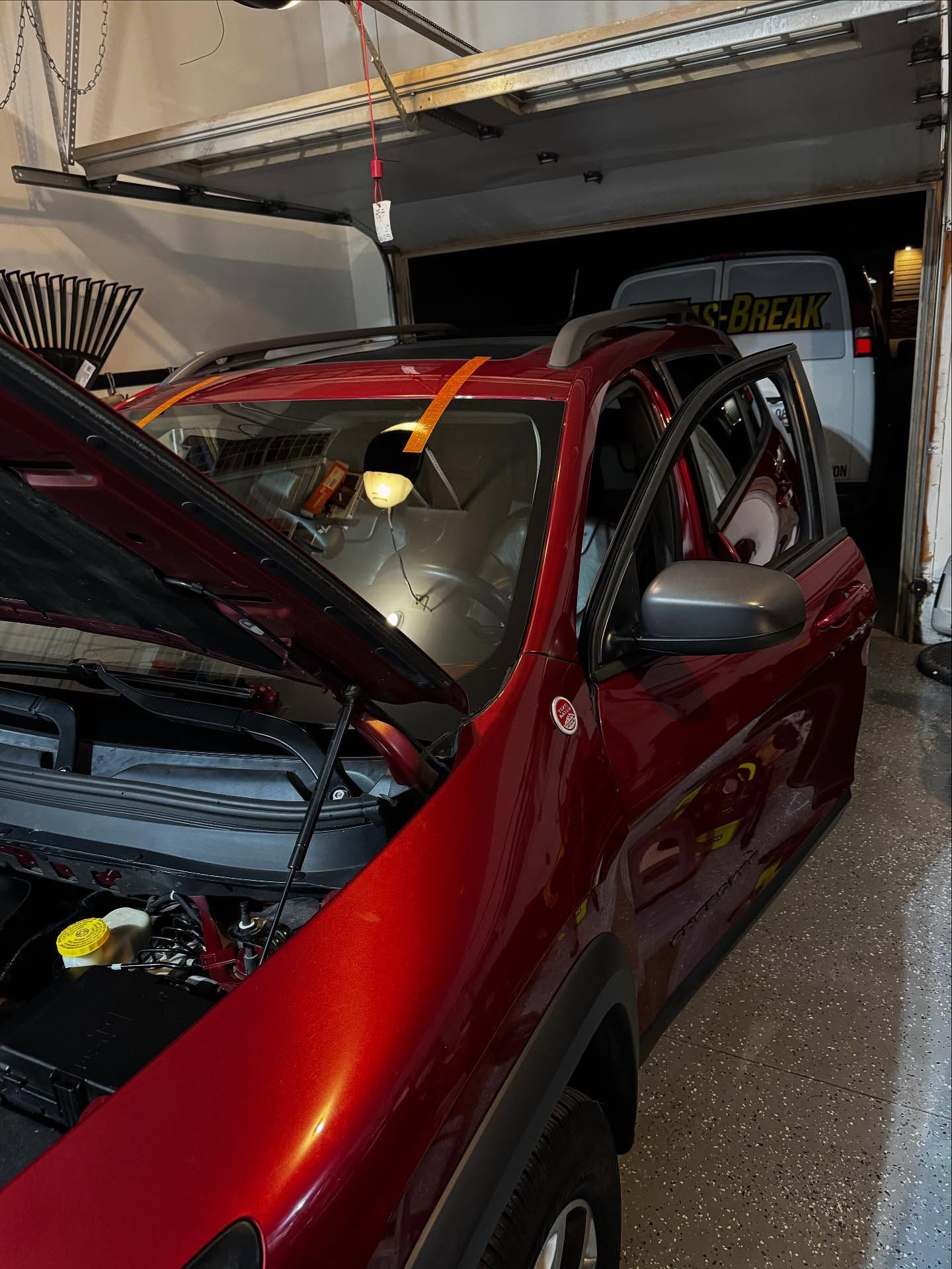 A dark red SUV with an open hood parked inside a garage, with a white van partially visible in the background.