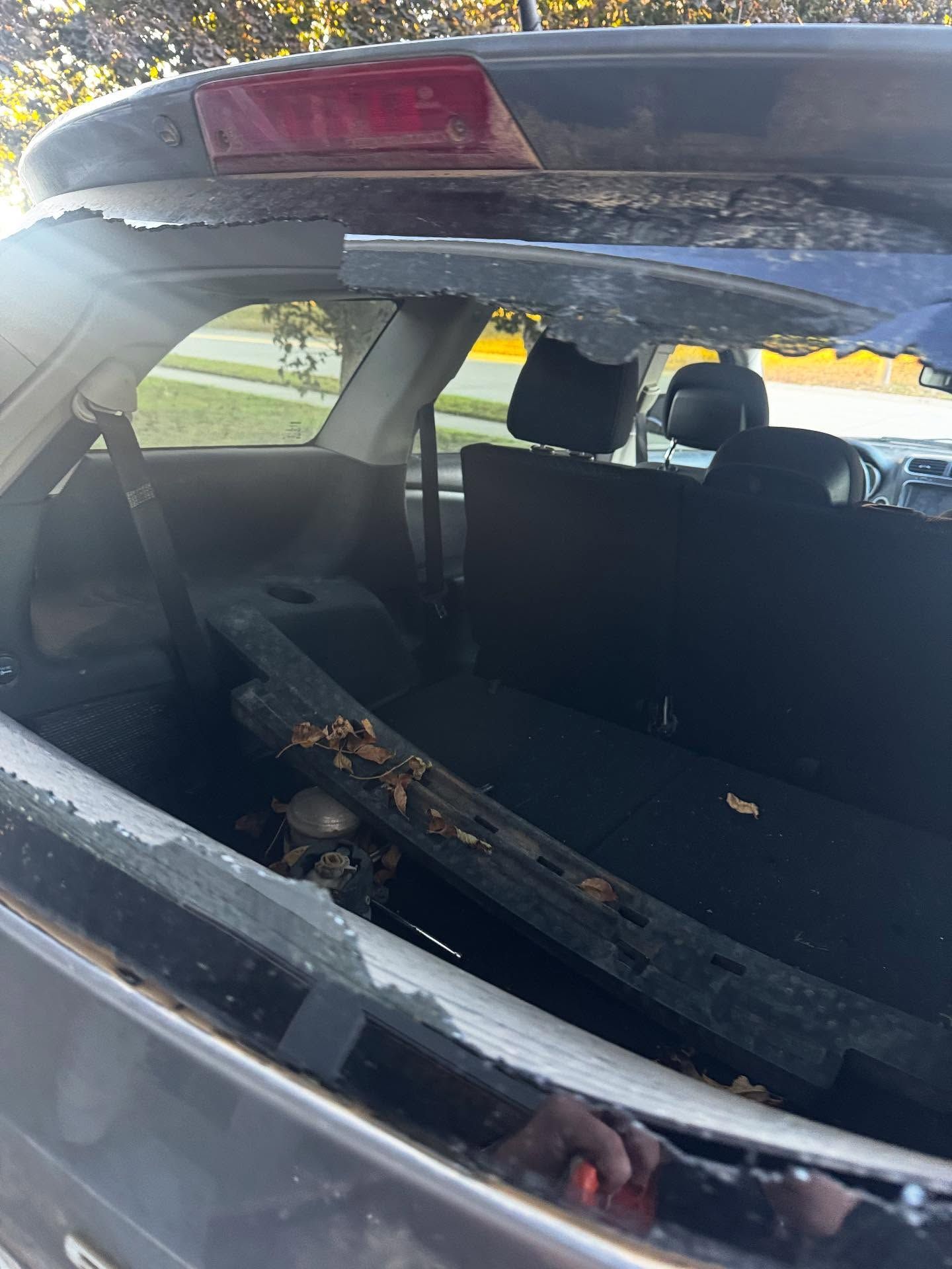 A shattered rear window on a dark-colored vehicle, with glass fragments scattered over the trunk cover and seats.