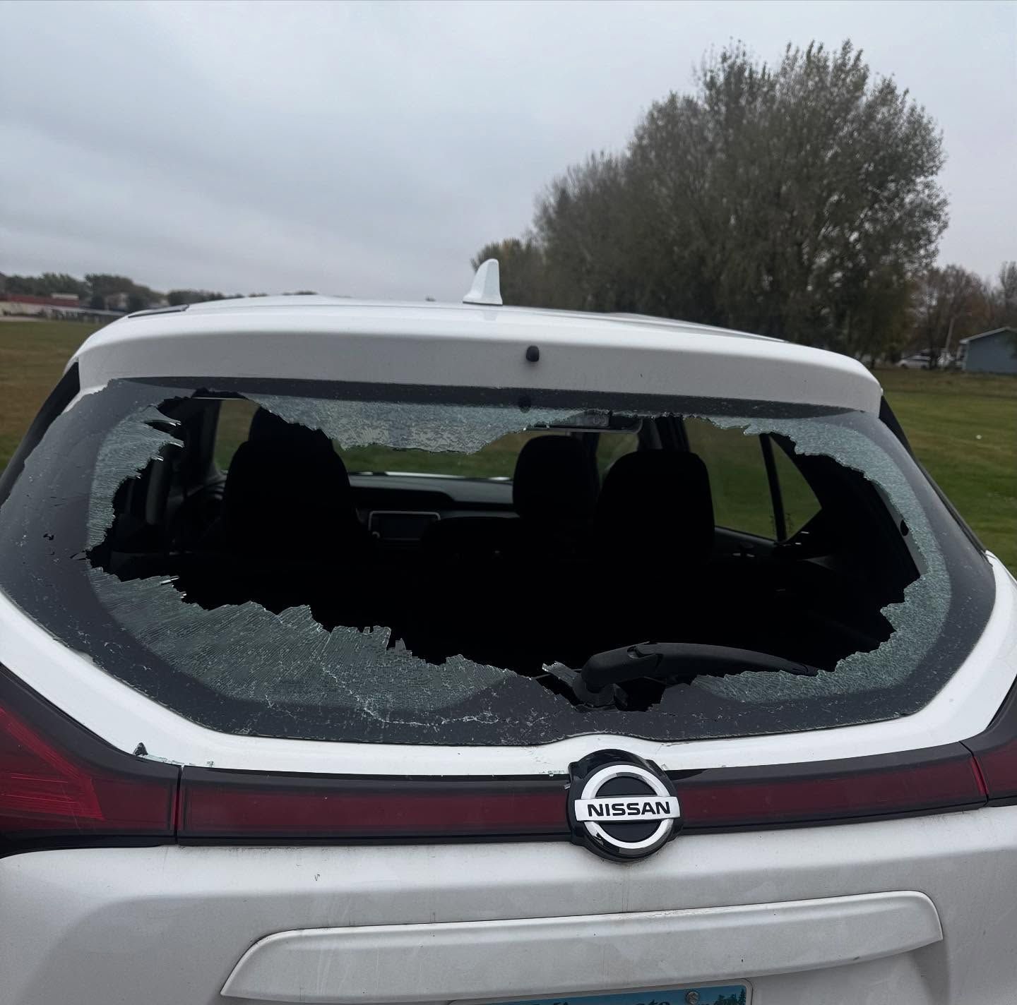 A white Nissan SUV with a shattered rear windshield, viewed from the back outdoors.