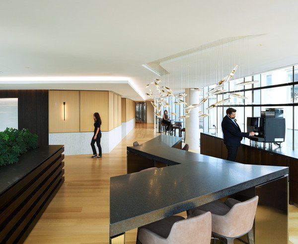 A man is sitting at a desk in an office while a woman walks by
