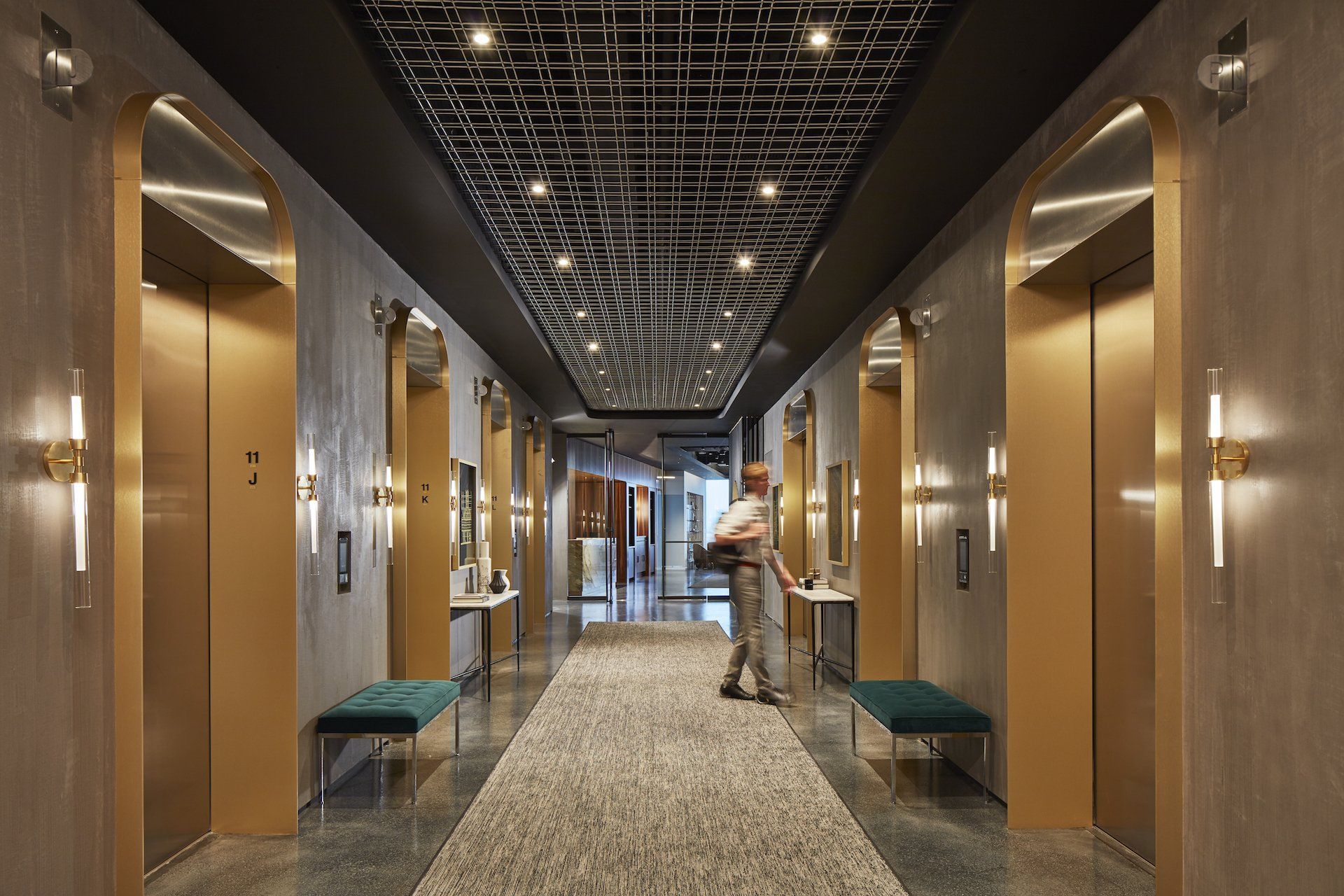 A man is walking down a hallway filled with elevators.