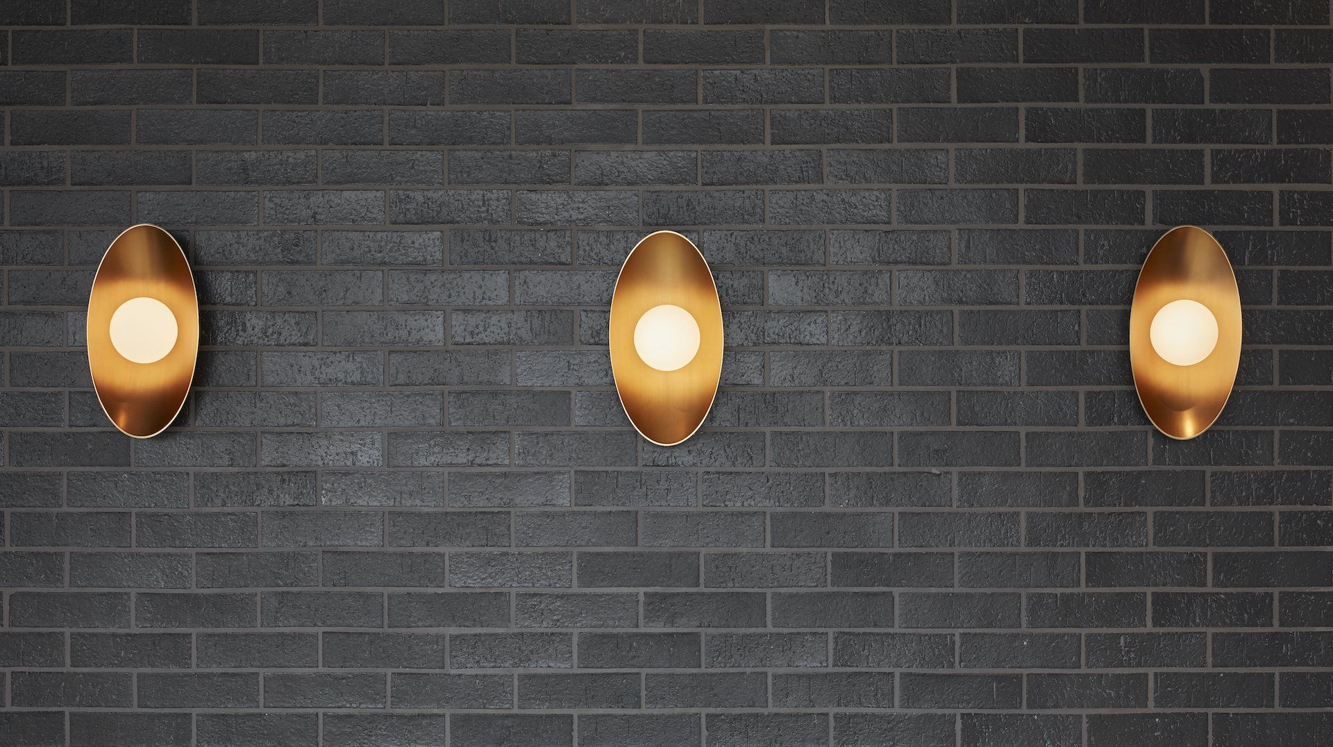 Three brass lights are hanging on a black brick wall.