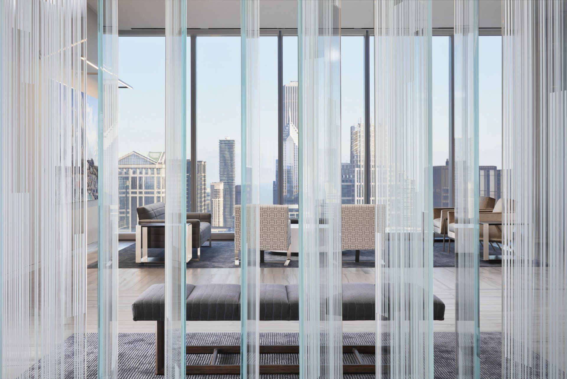 A living room with a bench and chairs behind a glass wall.