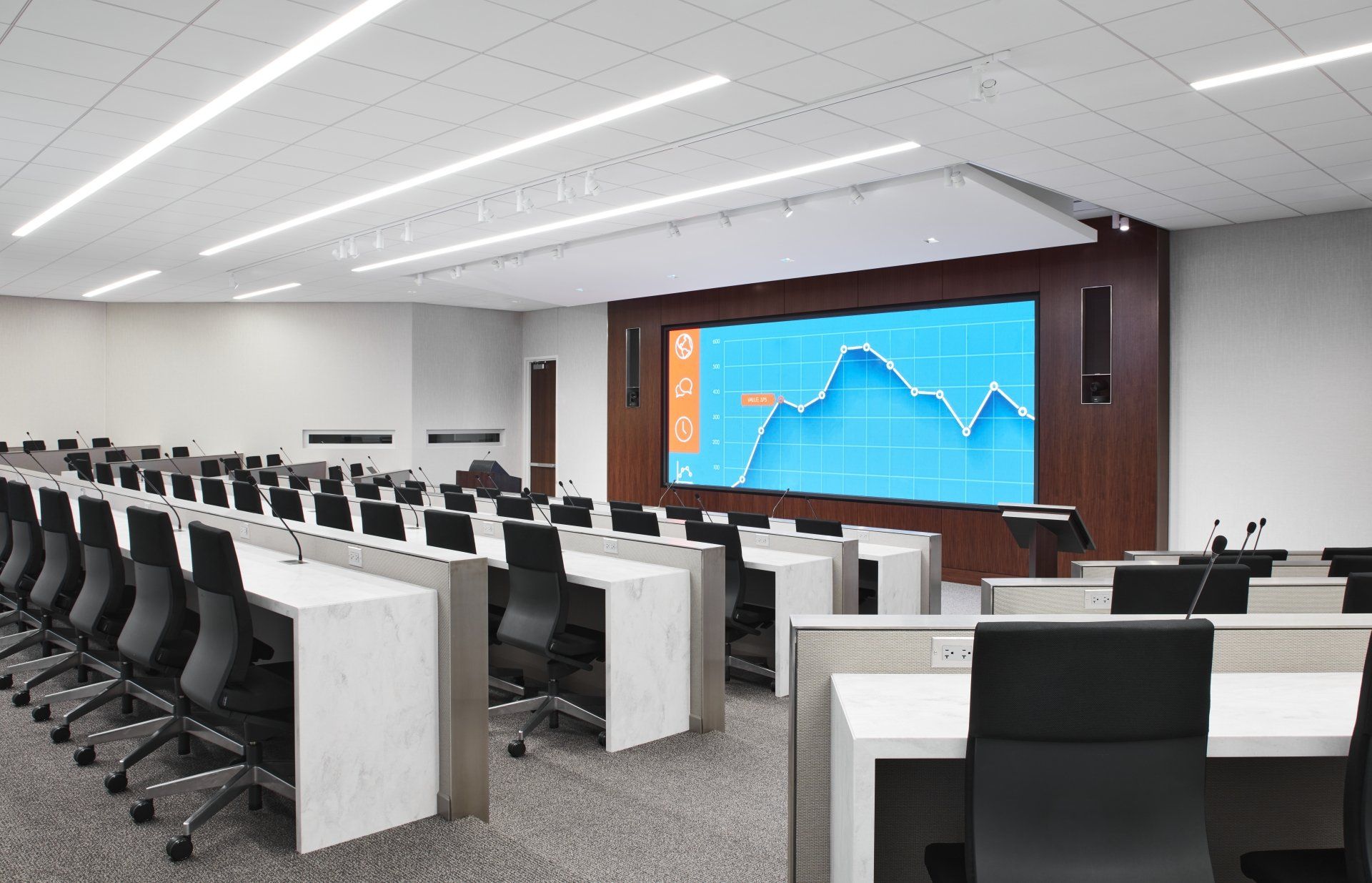 A large conference room with tables and chairs and a large screen on the wall.