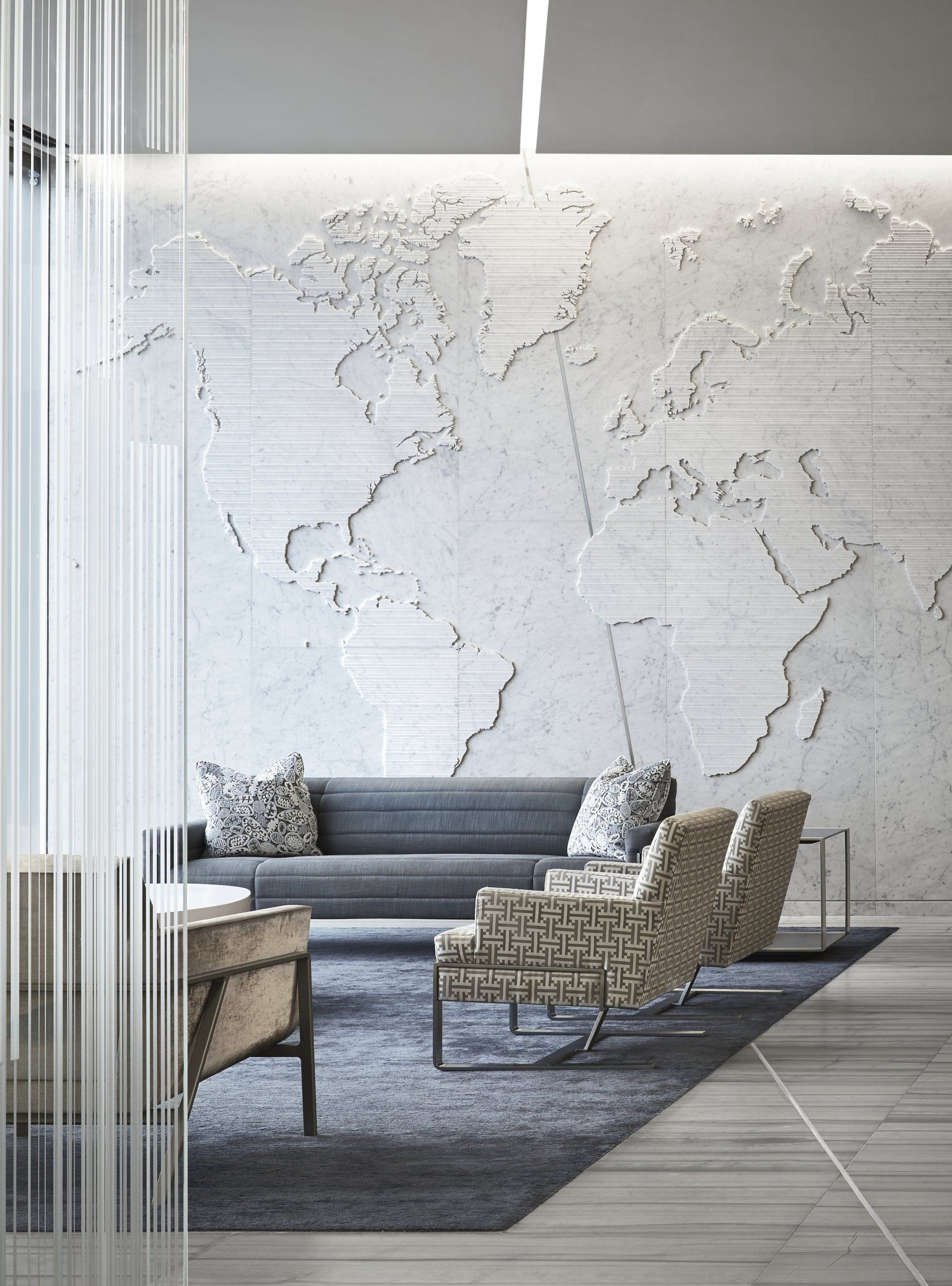 A living room with a couch , chairs , and a map of the world on the wall.
