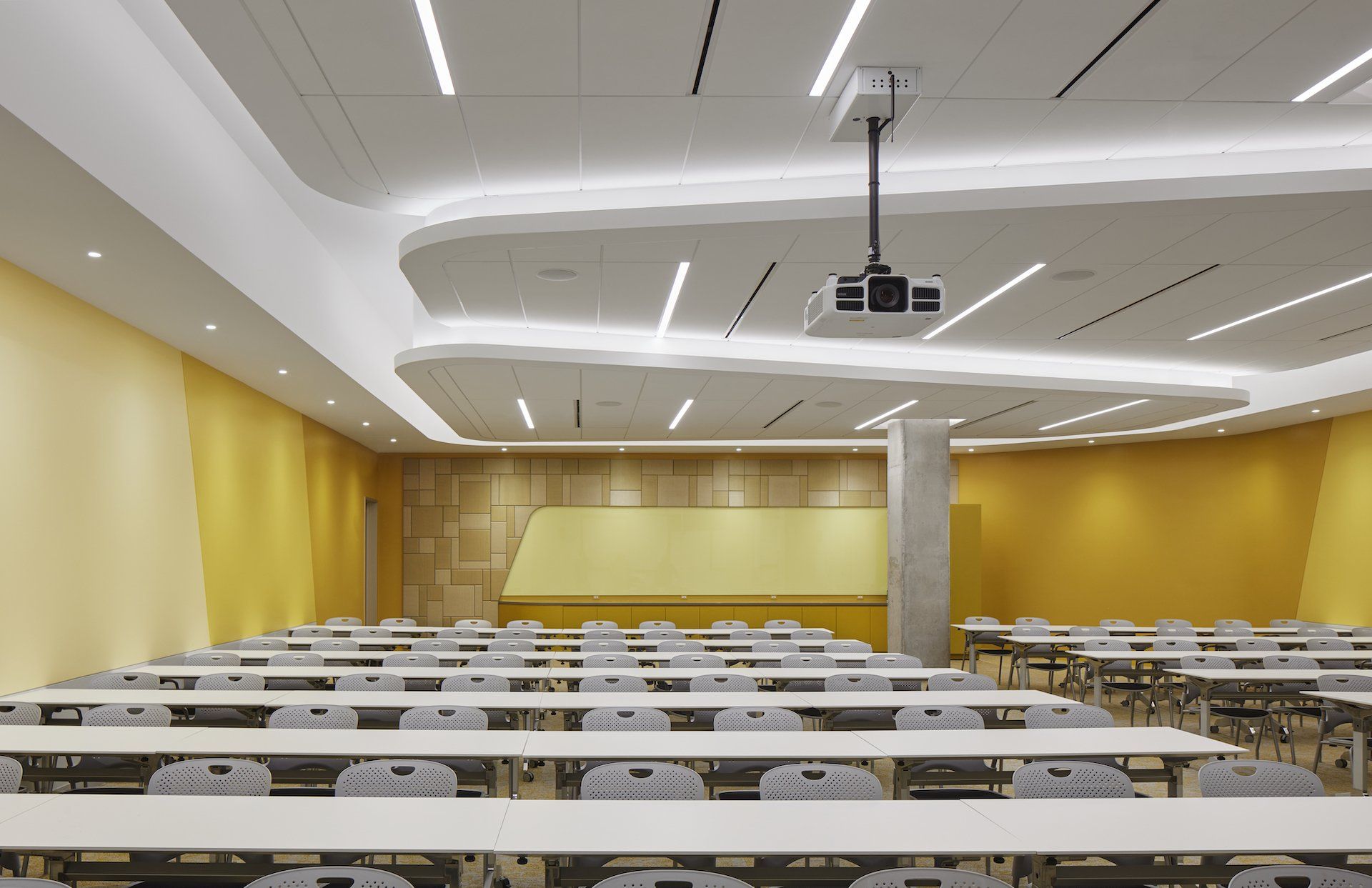 A large classroom with tables and chairs and a projector on the ceiling.