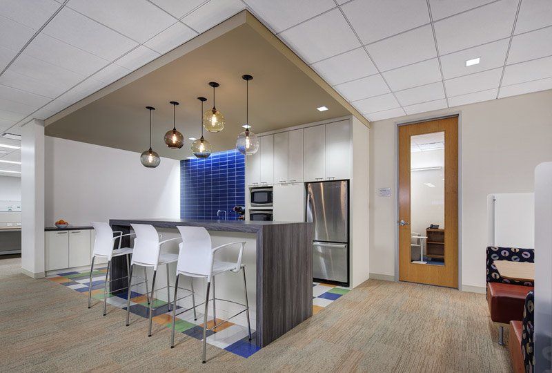 A kitchen with a large island and stools and a refrigerator.