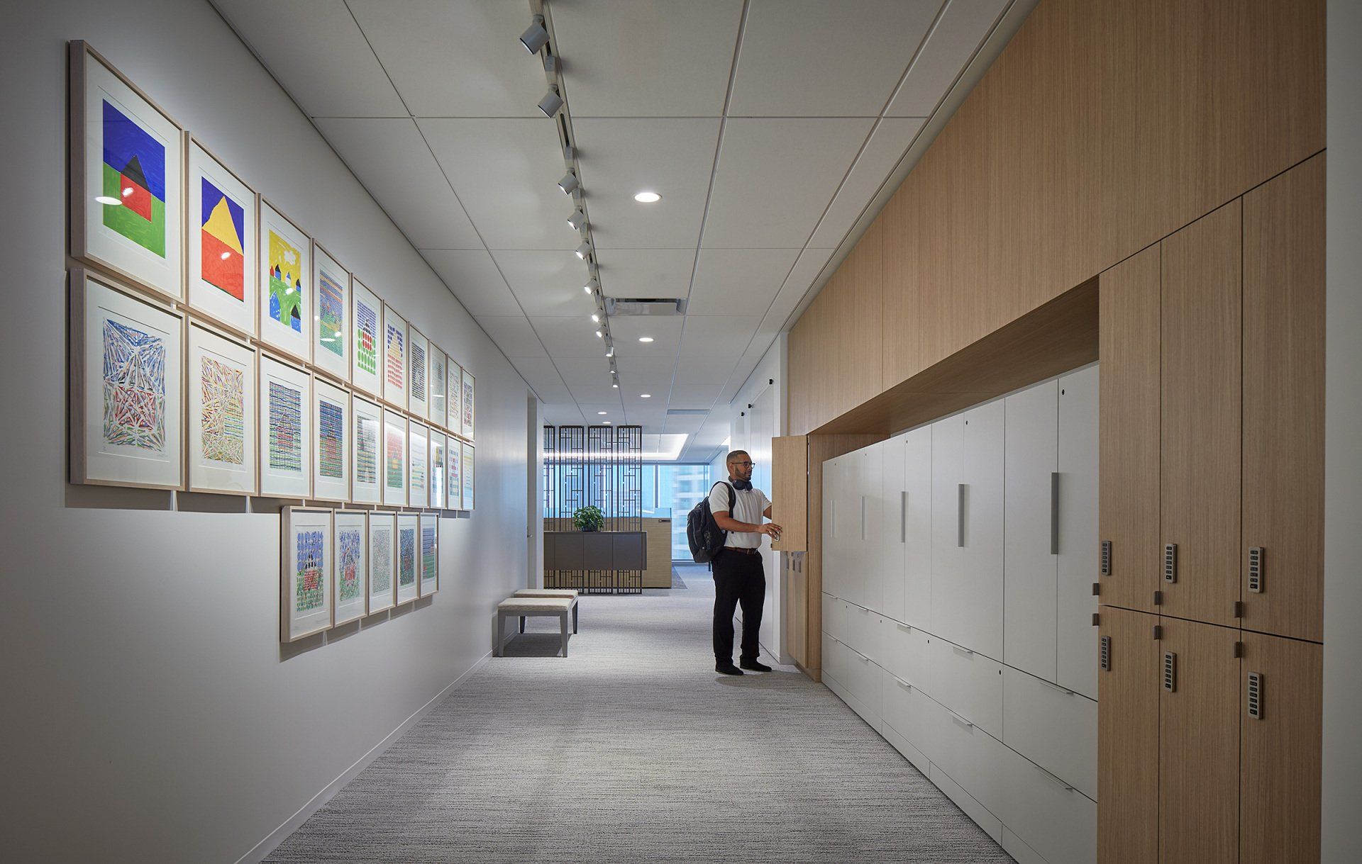 A man is standing in a hallway next to a row of lockers.