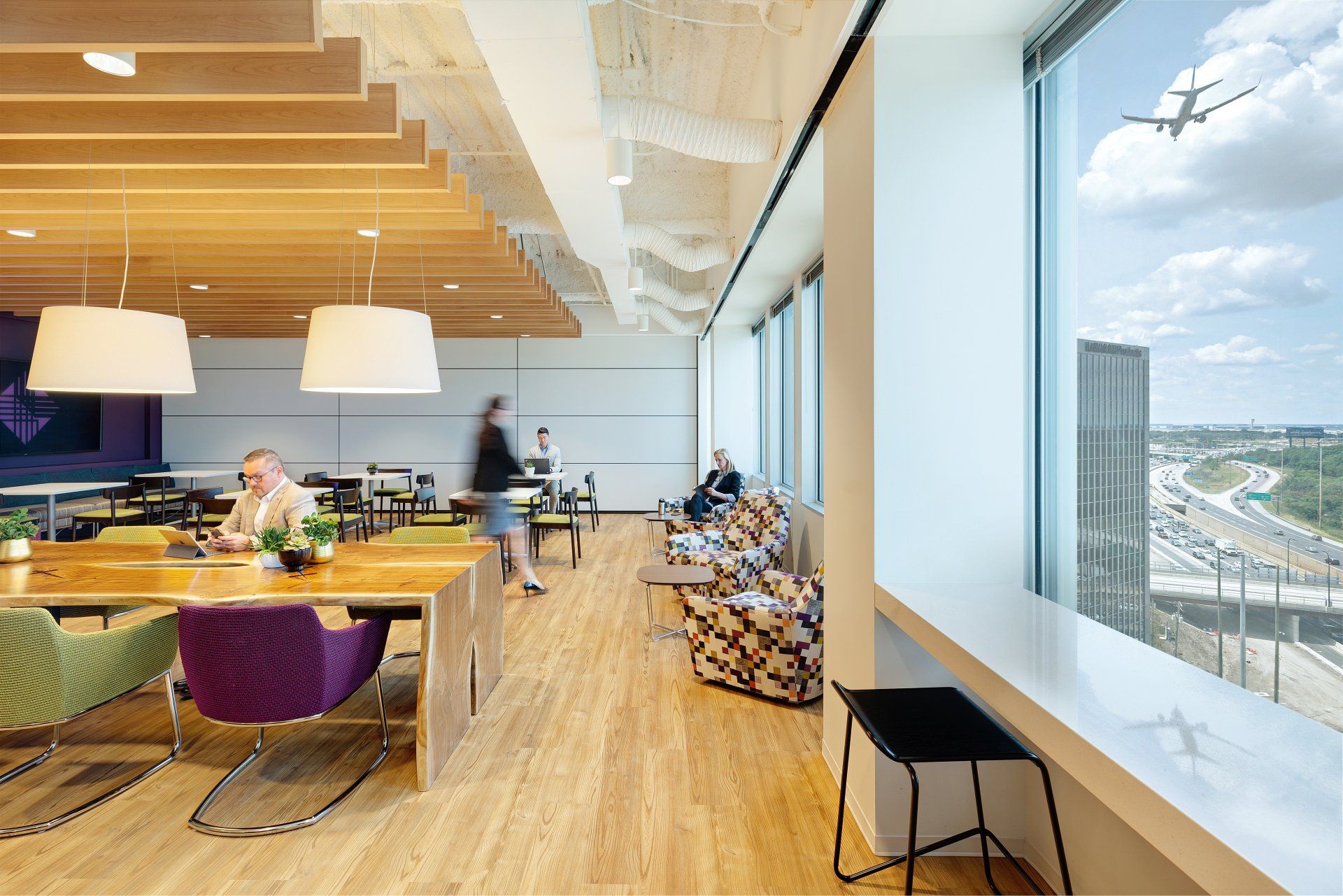 A group of people are sitting at tables in a room with a view of a plane flying overhead.