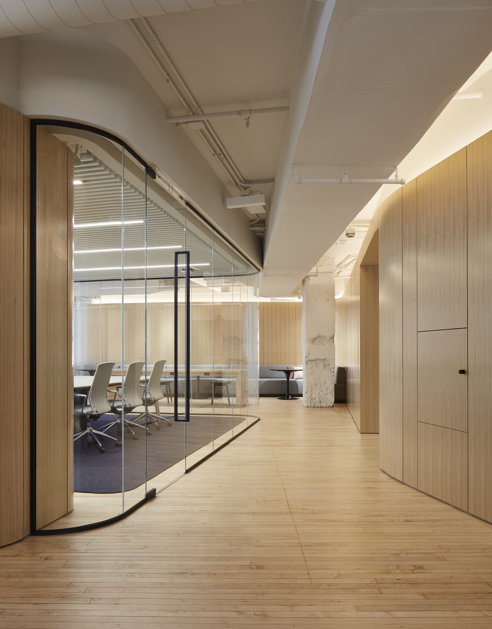 A hallway with wooden floors and a glass wall leading to a conference room.