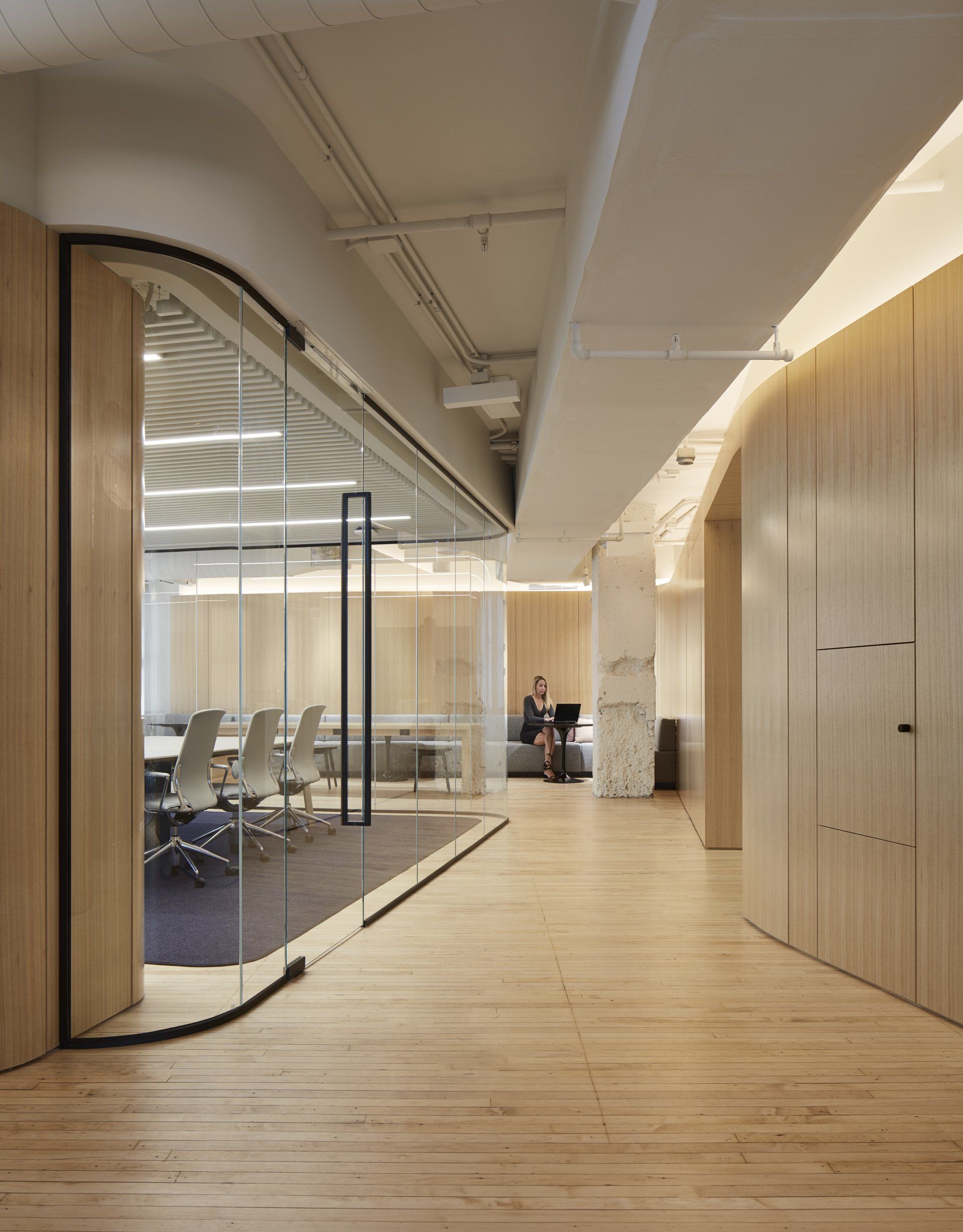 A woman is sitting on a couch in a conference room with a glass wall.