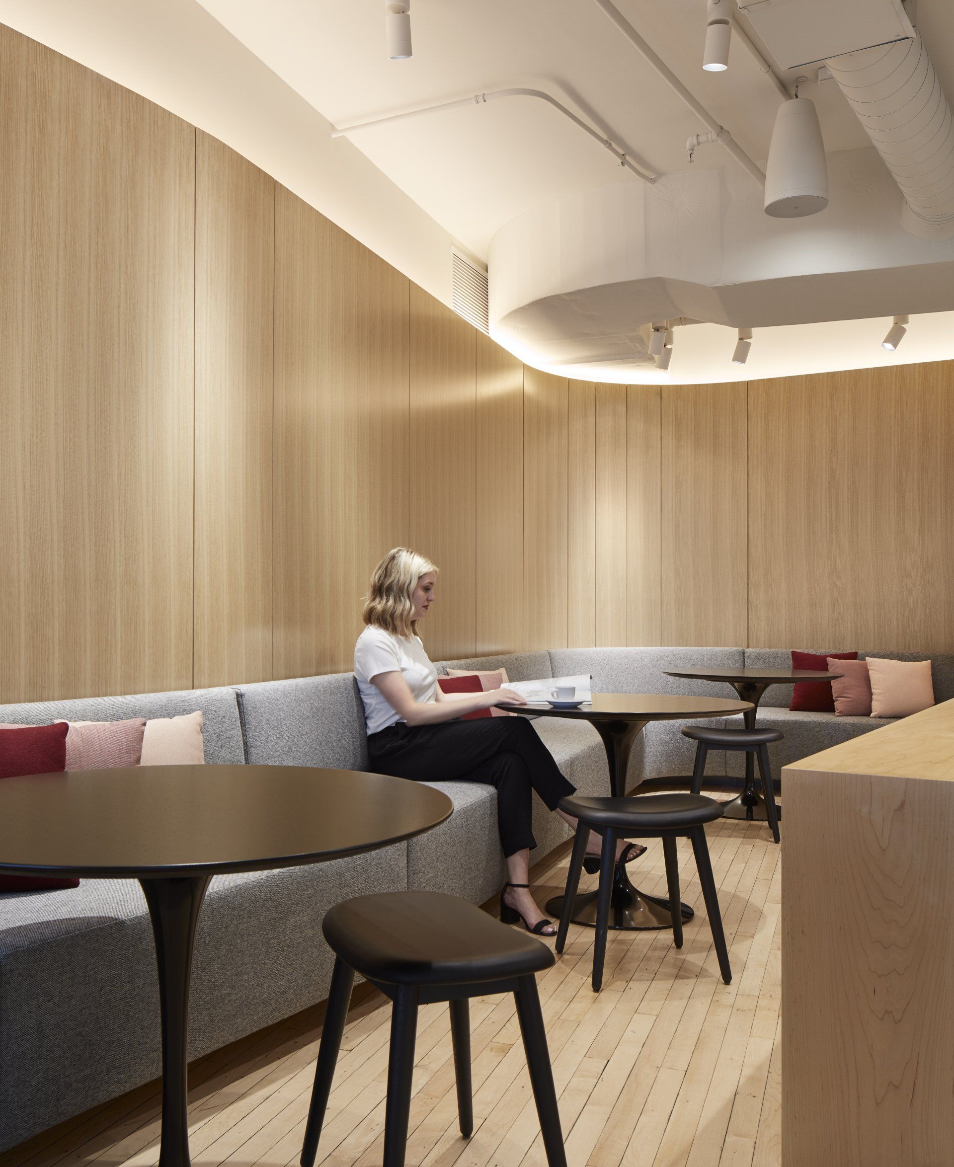 A woman is sitting on a couch reading a book in a room with tables and chairs.